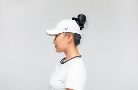 Girl with white ponyback ponytail hat on with hair in messy bun hat has p logo on the side