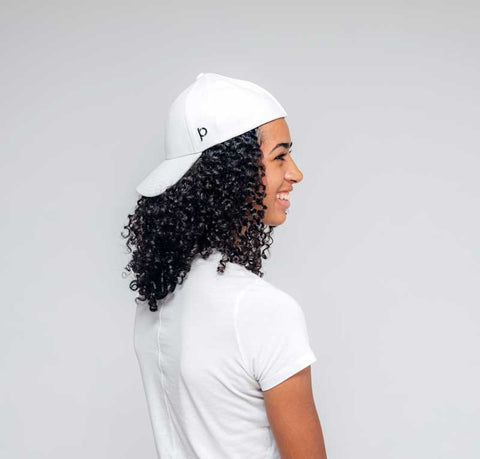 Woman with white ponyback baseball hat on backwards smiling away from camera