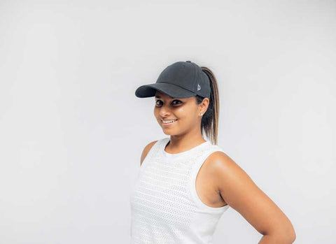 Woman wearing black high ponytail ponyback hat smiling at camera with grey background indoors