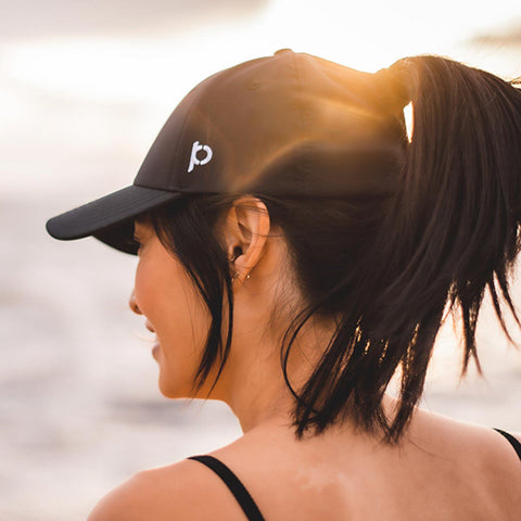 Woman smiling on beach with hair in a ponytail wearing a Ponyback Adventure Fit hat