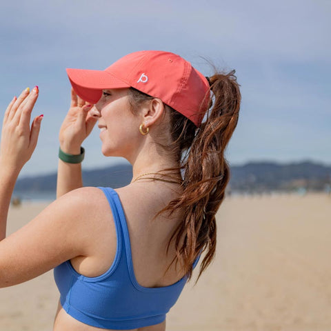 Woman wearing a coral Ponyback Ponytail Hat on the beach