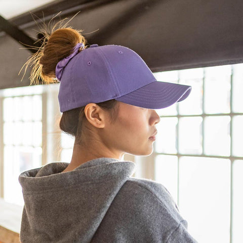 Woman wearing a violet purple Ponyback ponytail hat with a bun hairstyle