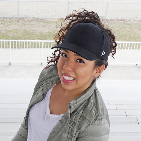 Girl with black high ponytail hat smiling in bleachers at field outside