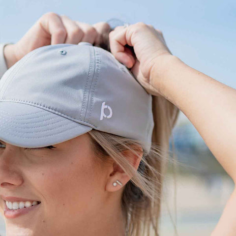 Woman adjusts her hair with a Grey Sporty Fit Ponyback ponytail hat