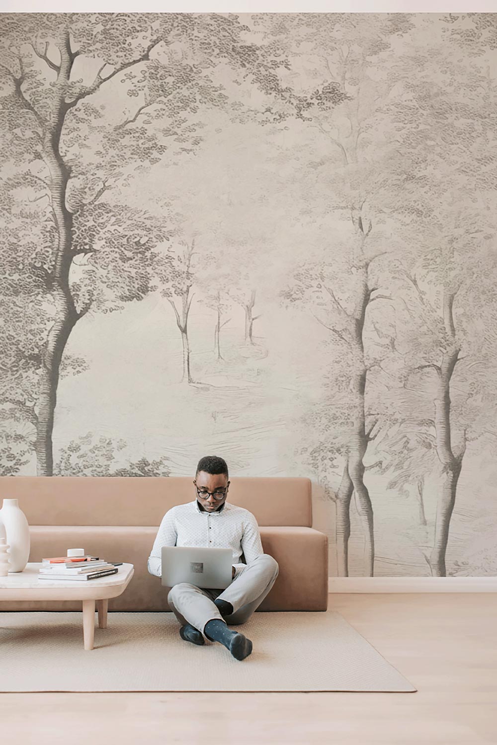 Man sitting on floor on laptop in front of couch. Birch Tree Wall Mural in background.