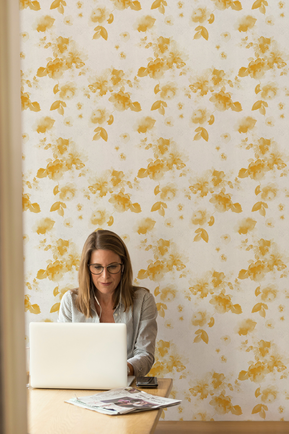 woman working on laptop in front of yellow floral wallpaper