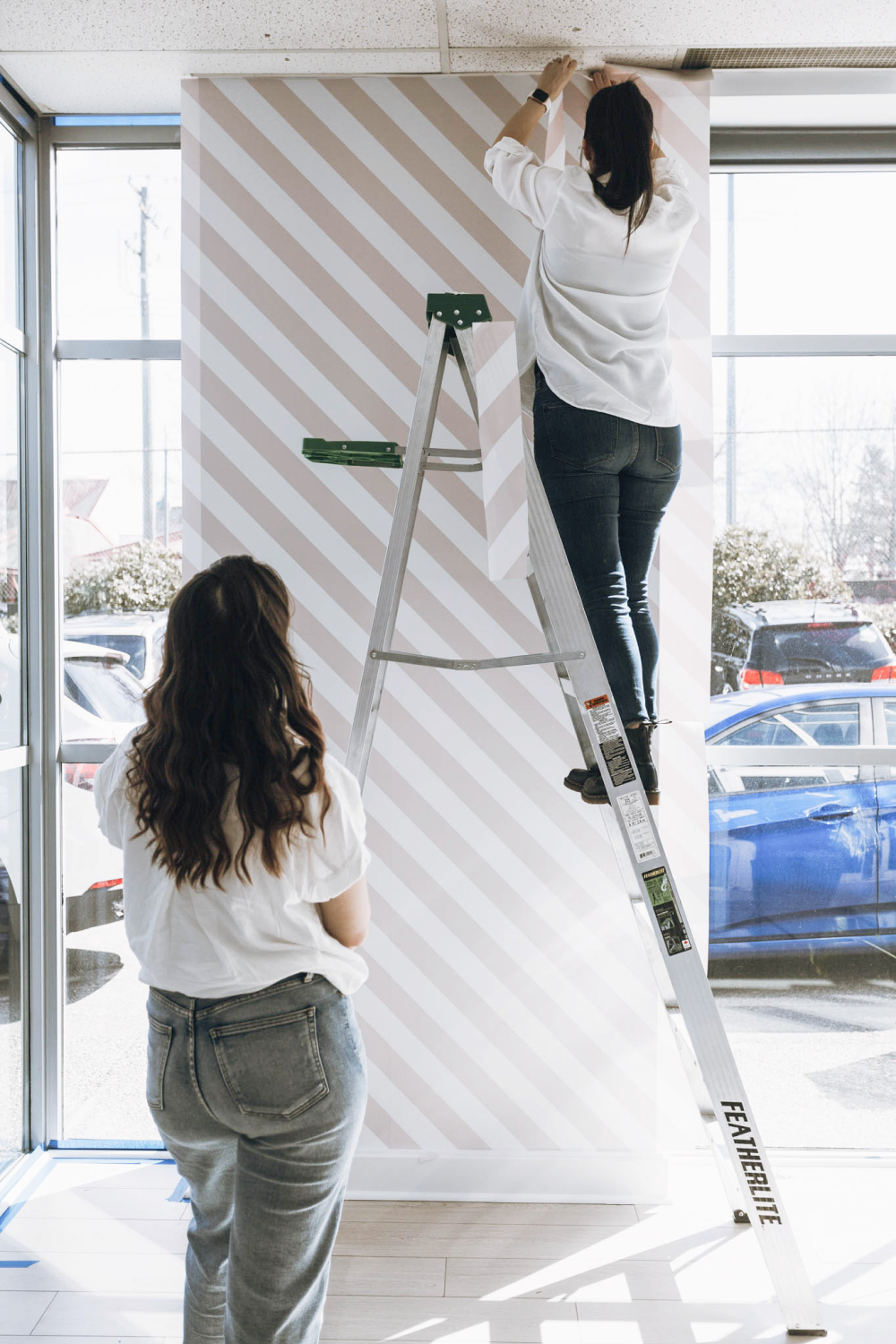 women installing custom pink striped wallpaper