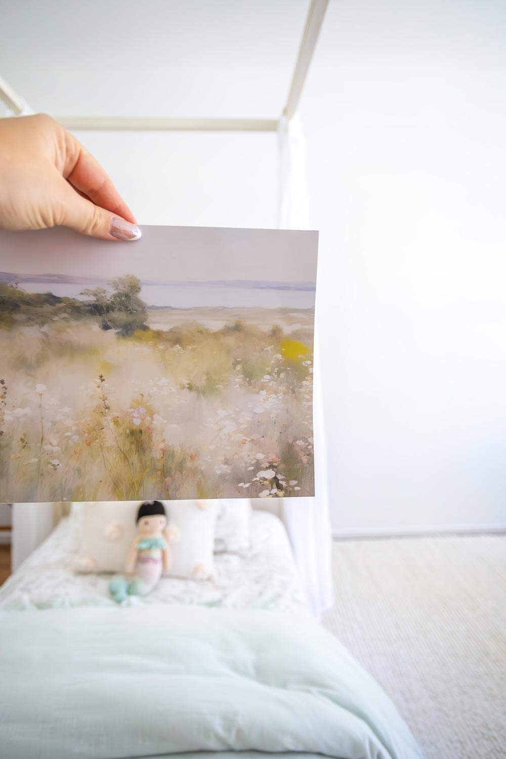 Hand holding a sample of the Watercolor Meadow Mural in front of shared girls bedroom.