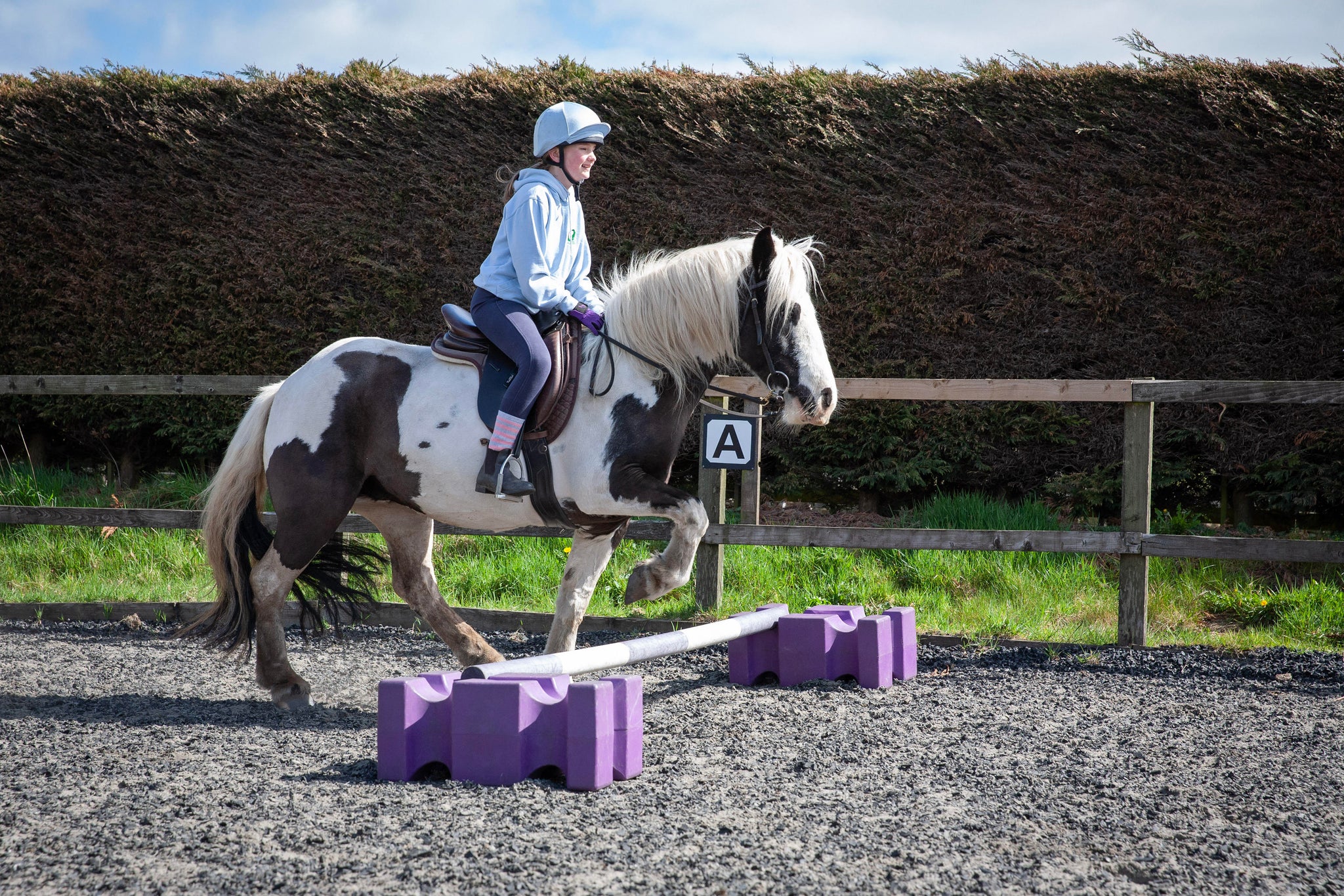 young girl riding a pony over a small jump