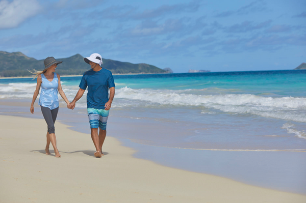 husband and wife walking on the beach in UPF swimwear and sun hats