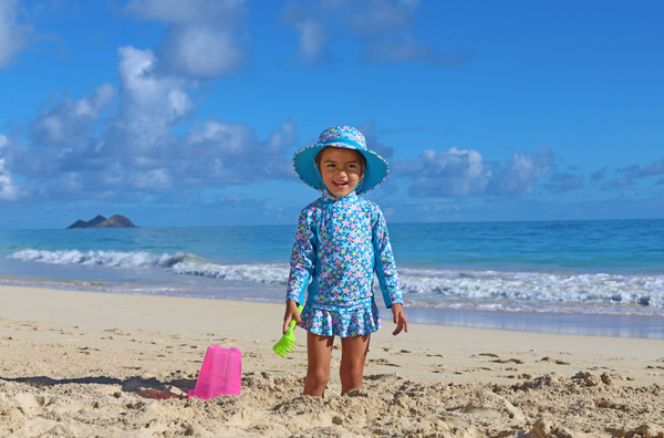 Little girl on the beach making a sand castle in a UPF swimsuit