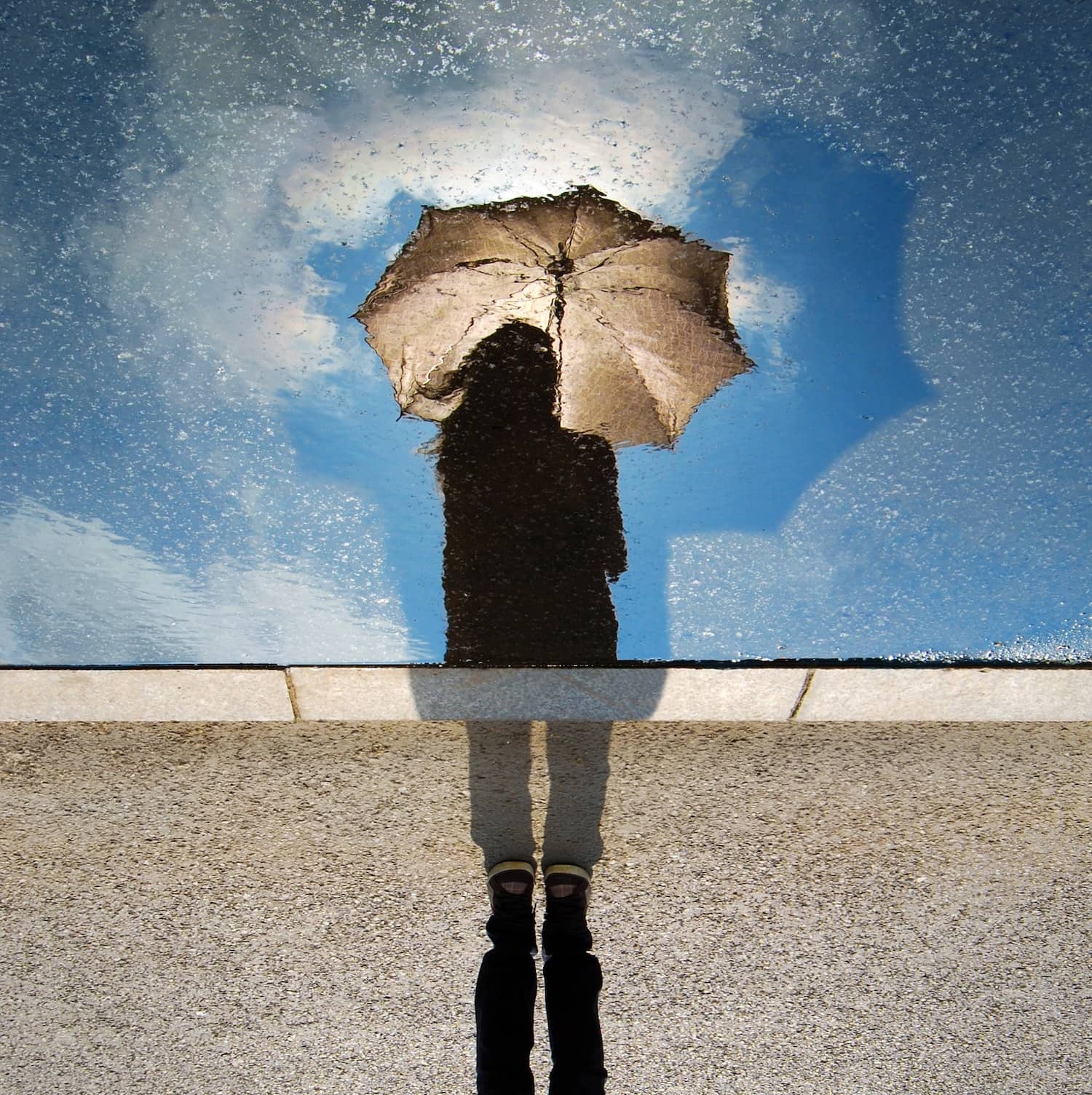 Riflesso in pozzanghera di una persona con un ombrello