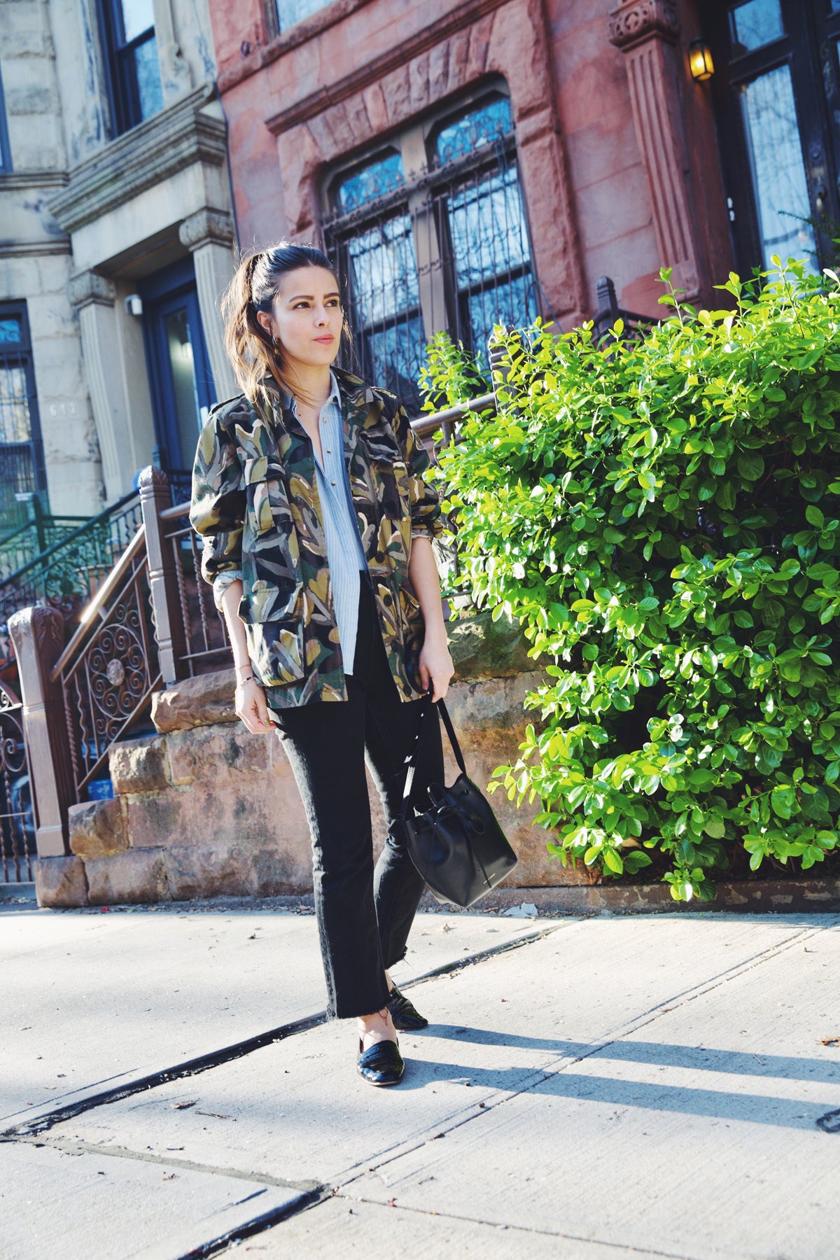 girl wearing camouflage jacket over blue and white striped shirt  with black jeans and black handbag