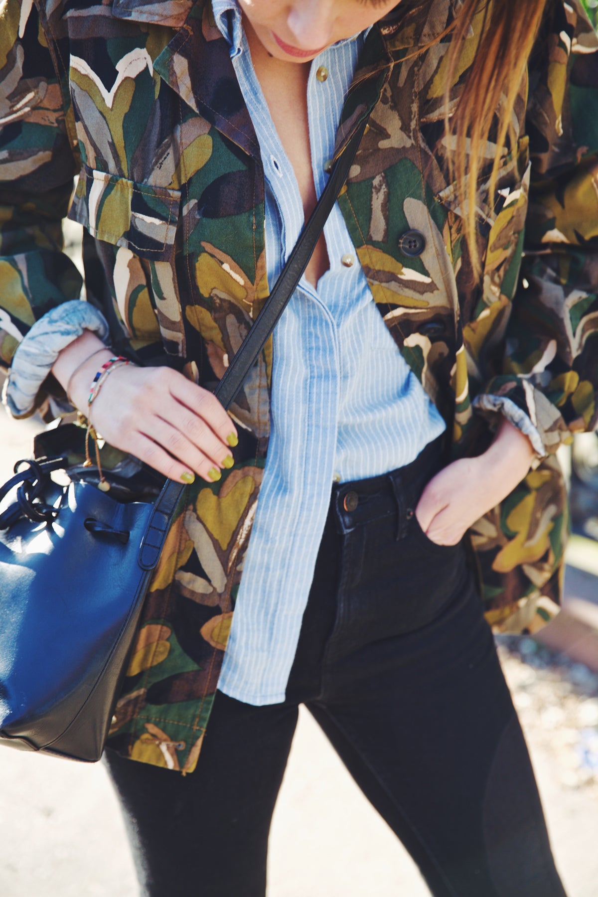 girl wearing camouflage jacket over blue and white striped shirt  with black jeans and black handbag