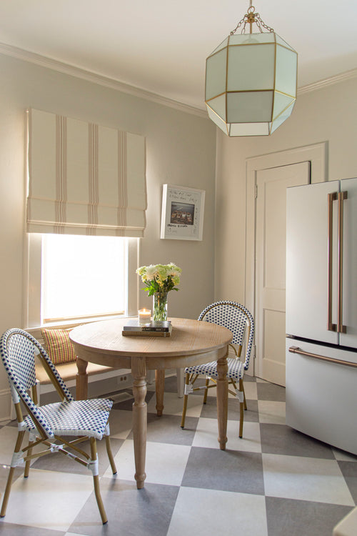 French inspired kitchen breakfast nook, with dining bench, round table, woven bistro chairs, glass lantern pendant, matte white and gold fridge by Atlanta interior design firm Kevin Francis