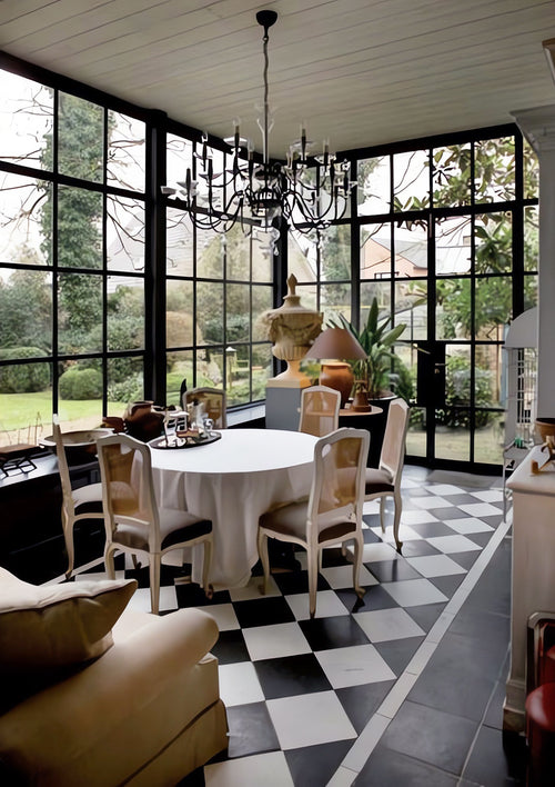 Glass sunroom dining room with steel framed windows, antique dining chairs, vintage chandelier, and black-and-white checkerboard tile flooring on Kevin Francis Design