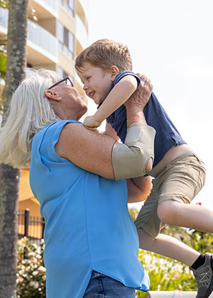 Grandmother holding her grandson while wearing the BioMagnetic Elbow Support in Beige.