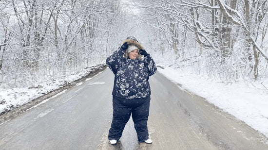 A plus size woman standing in snowy scenery wearing snow pants and snow jacket