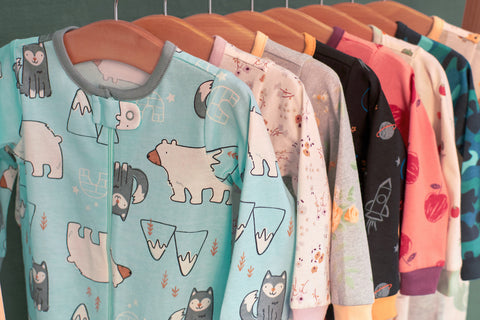 Row of baby footed pajamas hanging on a clothes rack, the first one is icy blue with polar bears