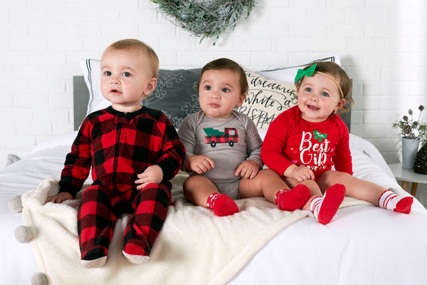 Three babies sitting on bed in Christmas pajamas