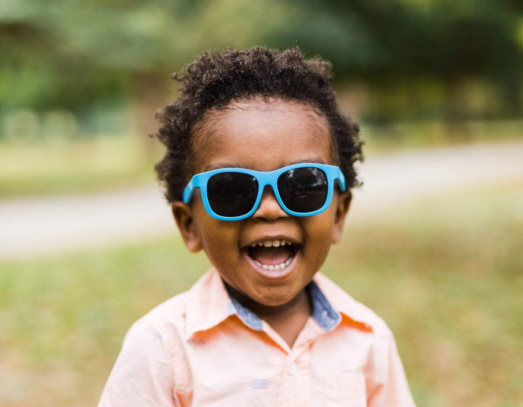 Baby boy smiling while wearing blue Babiators sunglasses