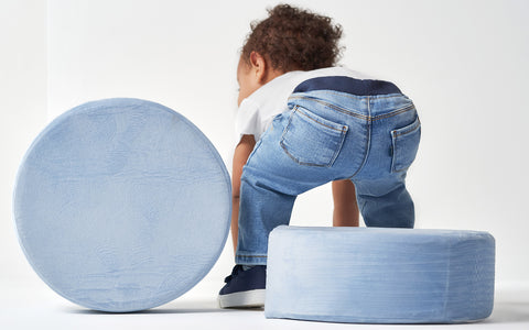 Baby bending over in blue jeans, playing with cushions