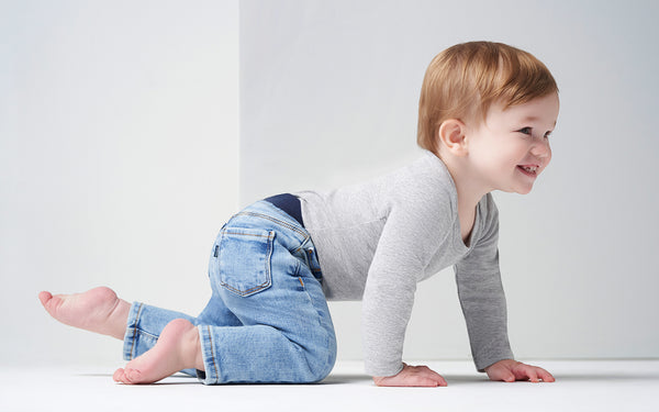 Baby boy in gray shirt and blue denim pants crawling across the floor