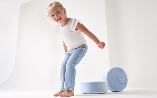 Toddler girl in blue jeans and white shirt jumping off blue cushion
