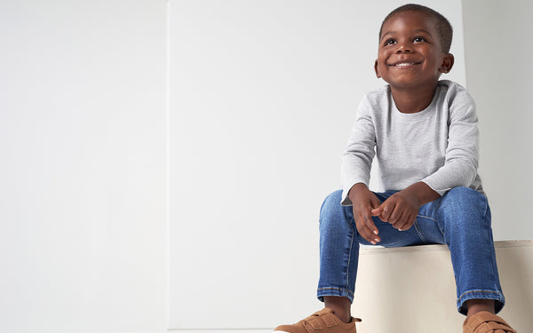 Toddler boy sitting on cushion in blue jeans and long sleeve gray shirt