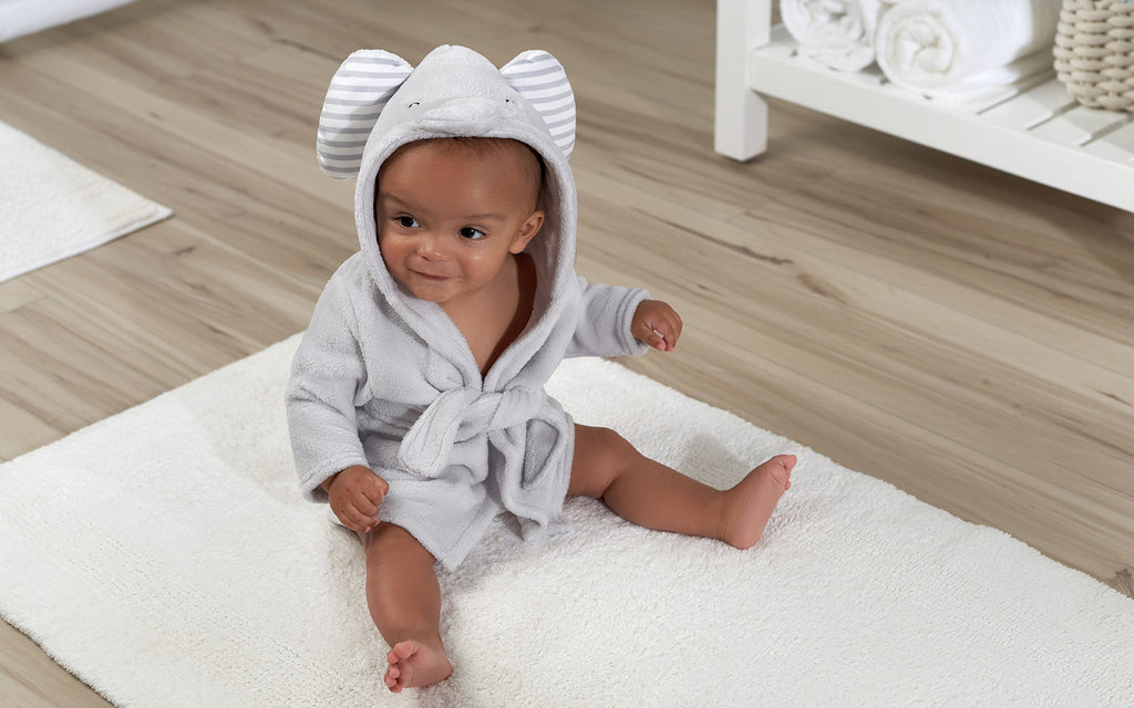 Cute baby in grey fuzzy robe sitting on a white cuddly rug.