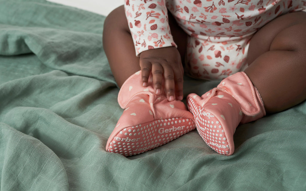 baby sitting on green blanket wearing pink booties