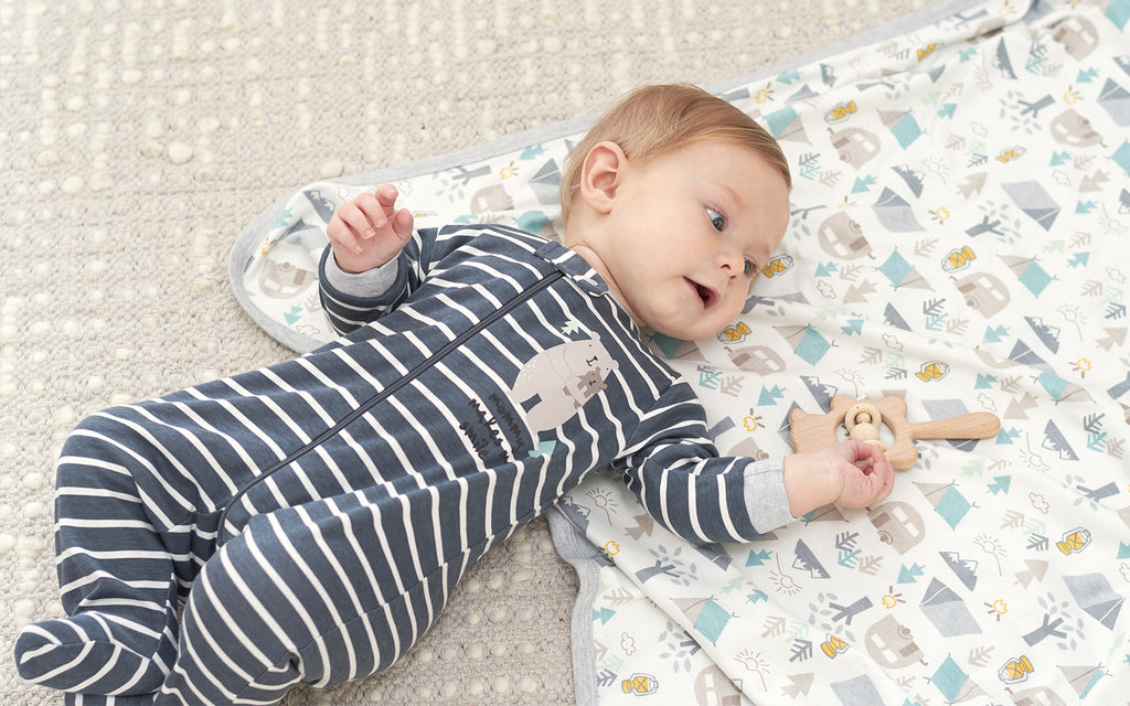 baby boy wearing striped pajamas lays on blanket, smiling