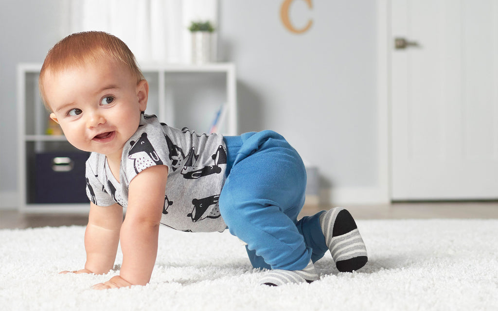 a baby crawls across the floor and smiles, facing camera