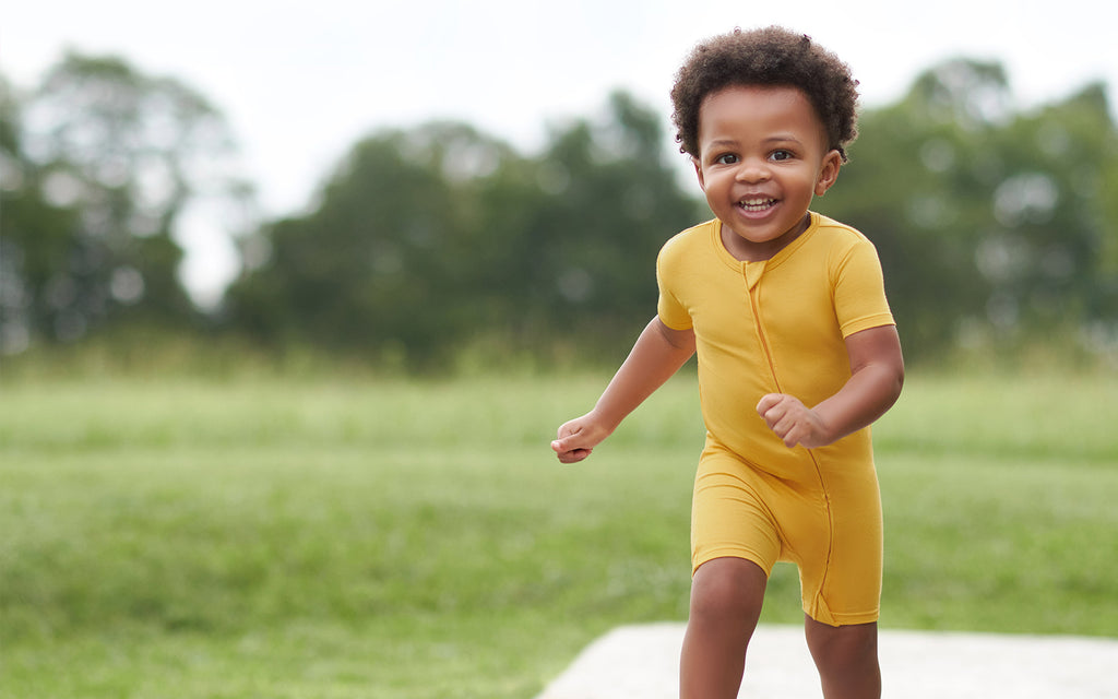 toddler boy in yellow romper running towards camera, smiling