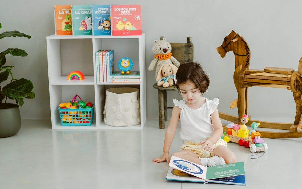 chidl sits on floor in nursery, reading a book by herself