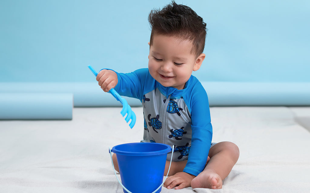 toddler boy in turtle rash guard playing with beach toys