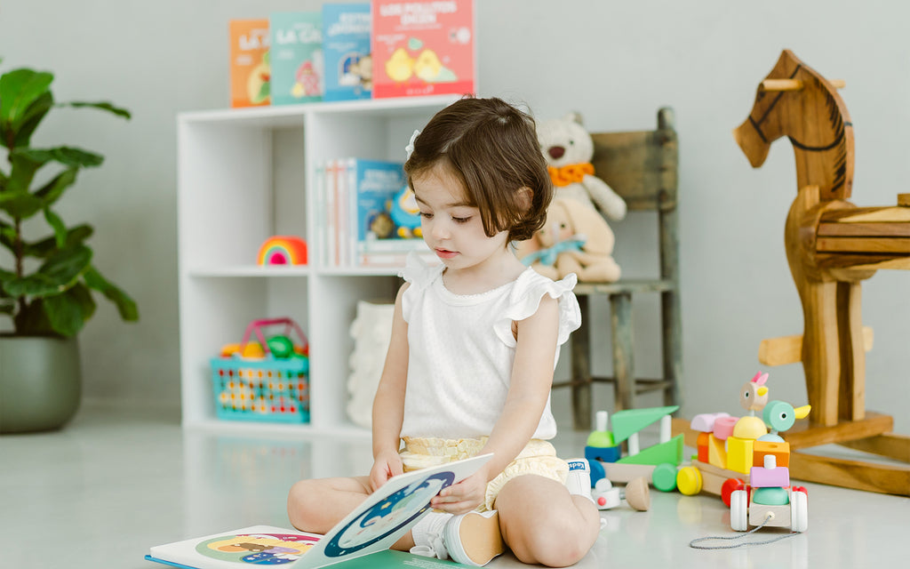 little girl sits reading in a play room with toys and books in background