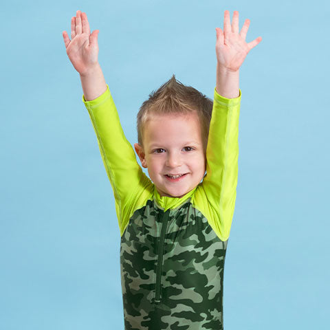 Baby boy standing with arms raised in green alligator swimsuit