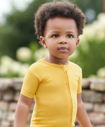 Toddler boy wearing honey yellow romper outside