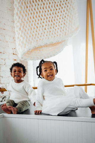 a smiling boy and girl dressed in white sit on counter