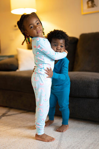 Young girl and her little brother stand in front of couch hugging each other.