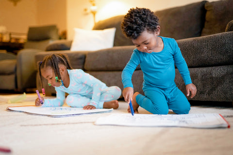 Young boy and sister sit in front of couch coloring