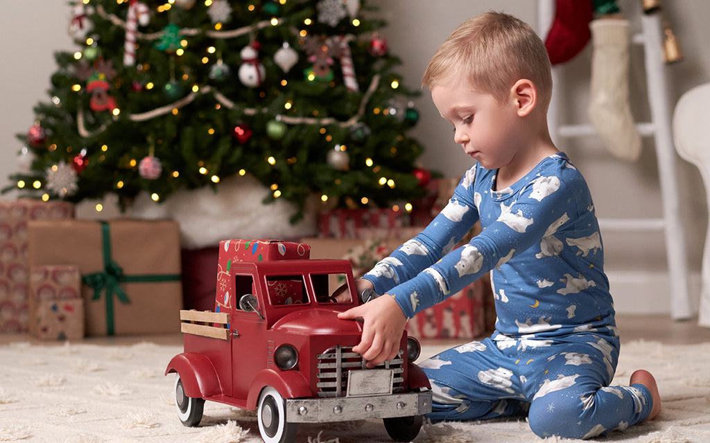 little boy in blue and white polar bear pajamas playing with red fire truck in front of christmas tree