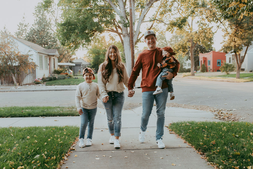 Mother, Father, and two boys walk down a street in fall. Father carries youngest.