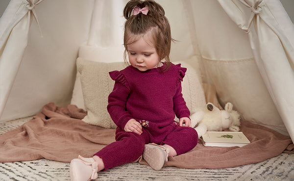 In an indoor play tent, a little girl in a matching outfit enjoys her time with a stuffed animal companion.