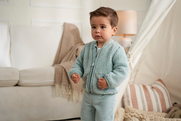 In a bright white room, a little explorer stands tall, sporting an adorable blue jacket.