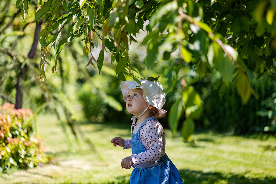 baby girl in denim dress stand under the tree in shade at sunny summer day