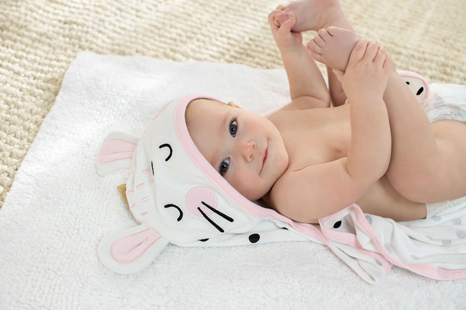 smiling baby girl laying down and grabbing her feet while wearing bunny towel