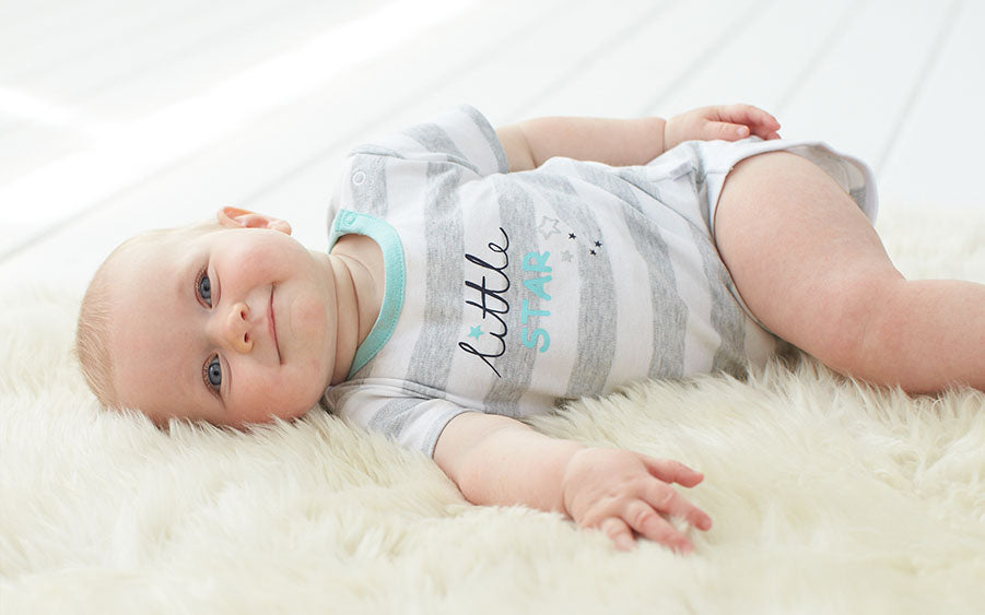 An endearing sight of a baby reclining on a white rug, wearing an adorable striped shirt.
