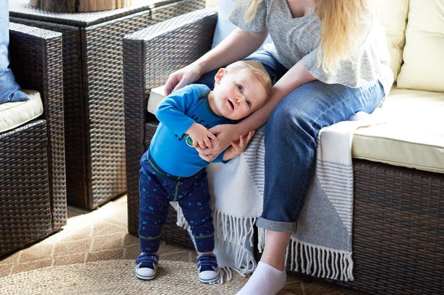 Baby boy wearing blue outfit leaning on his mother's lap.